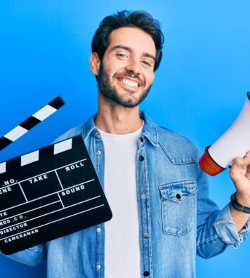 Young hispanic man holding video film clapboard and megaphone smiling with a happy and cool smile on face. showing teeth.