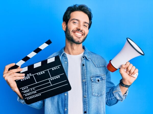 Young hispanic man holding video film clapboard and megaphone smiling with a happy and cool smile on face. showing teeth.